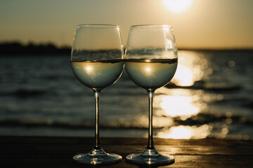 Two glasses of wine on wooden table near river at sunset