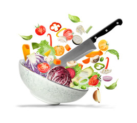 Knife, bowl and cut vegetables in air against white background