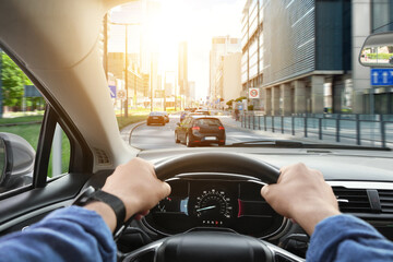 Driving car, view from driver's seat. Man holding hands on steering wheel, closeup
