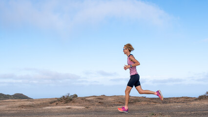 Fototapeta premium A slim woman runs on a dirt road with a blue shirt and pink shorts