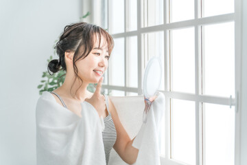 鏡で歯をチェックするアジア人女性（インプラント・ホワイトニング・歯列矯正）
