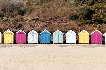 Row of wooden colorful beach huts in spring in sandy seafront with cliffs in background in Bournemouth, UK. South coast of England. No people.