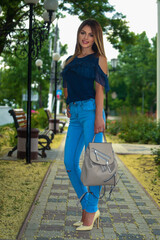 Portrait of a beautiful fashion model blonde girl in the nature with makeup and hairstyle against downtown in jeans