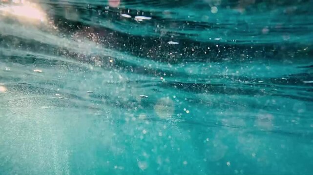 Sun rays and bokeh flicker in turquoise water from below the surface captured in slow motion