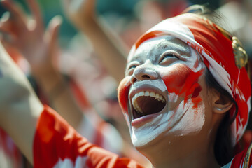 The face of a cheerful young woman is decorated with the colors of the Indonesian flag. Shouting and raising hands in joy Celebrate freedom and independence day.