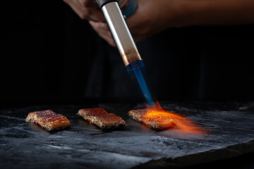 Japanese food chef using kitchen torch burn on Unagi Eel Nigiri Sushi (Eel Sushi) Japanese food...