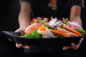 Close up, Japanese food chef serves a set of traditional Japanese sashimi beautifully arranged on a fishing boat-shaped bowl