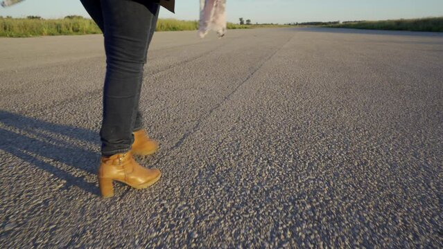 Piernas y perfil de una mujer andando por una pista de aterrizaje hacia el infinito o el futuro.