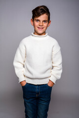 Portrait of a smiling young boy in jeans and a sweater, standing with his hands in his pockets