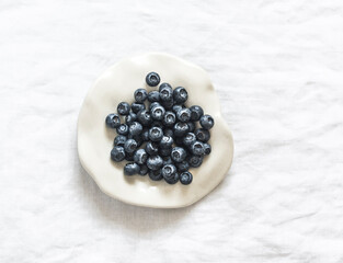 Fresh blueberries on a white ceramic plate on a light background, top view