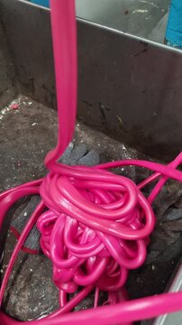 Pink rubber tubing melted being fed into a extrusion machine. The tubing is coiled and tangled, and it appears to be a manufacturing process. 