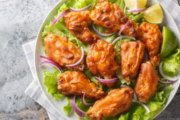 Tom yum chicken wings deep fried served with onions and lime close up in a plate on the table. Horizontal top view from above