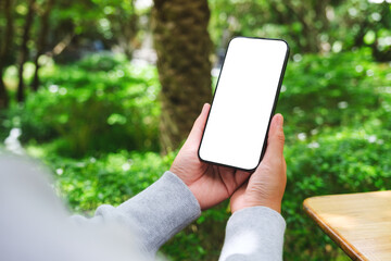 Mockup image of a woman holding mobile phone with blank white desktop screen in the outdoors