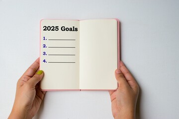 Hand holding a diary written 2025 Goals with numbers on a paper on white background. New year goals