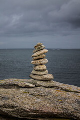 of balanced stones on a rocky shore with a cloudy sky in the background.