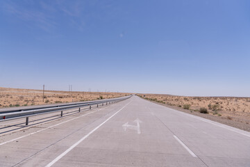 A long, empty road with a white arrow on the pavement. The sky is clear and blue