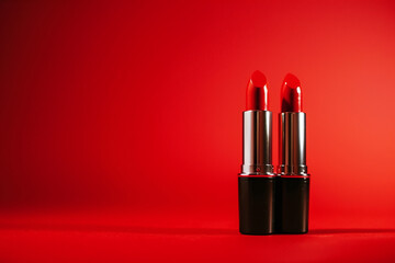 Red lipstick on a vivid red background with copy space. Cosmetics banner concept, top view, flat lay. Minimal and luxury make up cosmetic or beauty salon composition