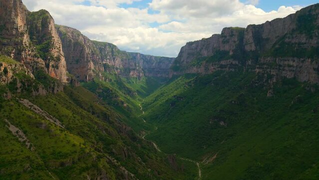 A breathtaking aerial view of Vikos Gorge in Greece, showcasing the lush green valley carved by the meandering Voidomatis River. The towering cliffs and dramatic landscape create a majestic scene.