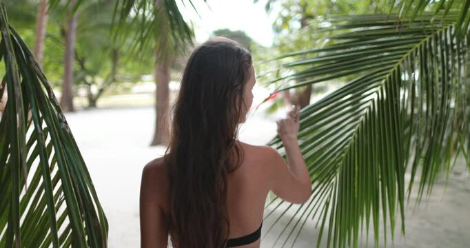 A woman in a black bikini is standing next to a palm tree in Thailands tropical setting.