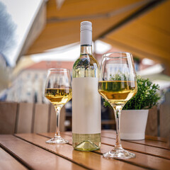 Bottle of chilled white wine and two glasses sitting on a wooden table in an outdoor restaurant