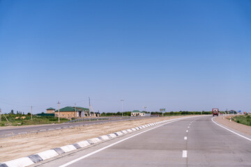 Fototapeta na wymiar A long road with a truck driving down it. The sky is clear and blue. There are no other vehicles on the road