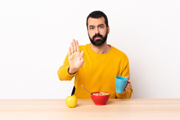 Caucasian man having breakfast in a table making stop gesture.