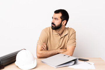 Caucasian architect man with beard in a table keeping the arms crossed.