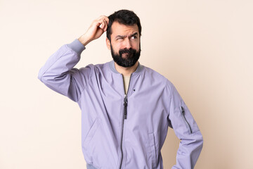 Caucasian man with beard wearing a jacket over isolated background having doubts while scratching head