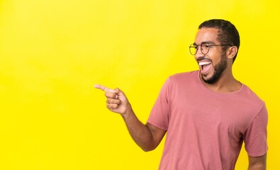 Young latin man isolated on yellow background pointing finger to the side and presenting a product