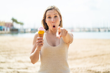 Young blonde woman with a cornet ice cream at outdoors surprised and pointing front