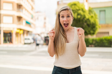 Young blonde woman at outdoors celebrating a victory in winner position