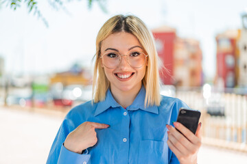 Young pretty blonde woman using mobile phone at outdoors with surprise facial expression