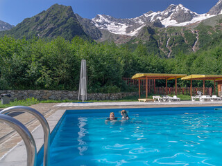 Family vacation in the pool. Relaxing by the water in the fresh air. Mom and daughter swim in the outdoor pool in summer. Vacation in the mountains in summer.