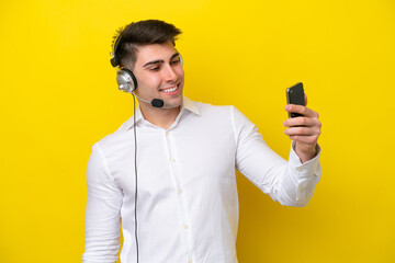 Naklejka premium Telemarketer caucasian man working with a headset isolated on yellow background making a selfie