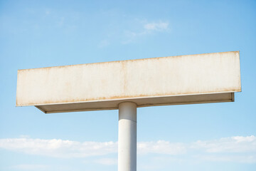 A blank billboard with a weathered white surface against a blue sky with white clouds. The billboard is mounted on a white pole. This image is perfect for any project that needs a blank canvas to add 