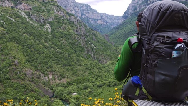 A breathtaking view of the Vikos Gorge in Greece, showcasing a lush, green landscape with a single hiker traversing the distant trail.