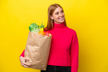 Young redhead woman holding a grocery shopping bag isolated on yellow background thinking an idea while looking up