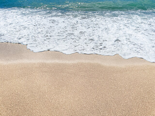 Natural background. Seascape. A sandy smooth beach. A sea wave on the sand. Smooth, clean sand. Summer background. View from above. Close-up. Copy space