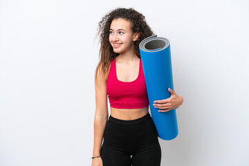 Young sport Arab woman going to yoga classes while holding a mat isolated on white background looking to the side and smiling