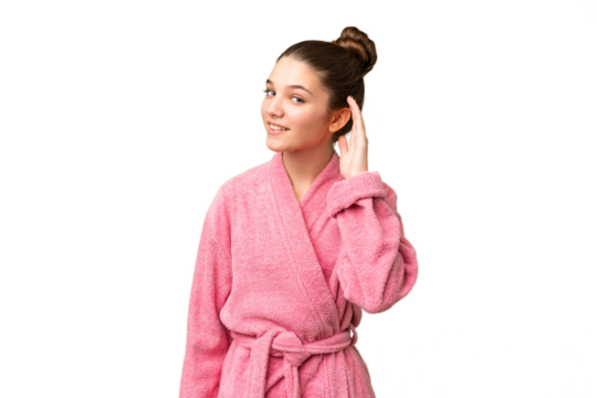Teenager girl in a bathrobe over isolated chroma key background listening to something by putting hand on the ear