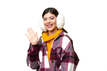 Young Russian woman wearing winter muffs over isolated chroma key background saluting with hand with happy expression