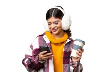 Young Russian woman wearing winter muffs over isolated chroma key background holding coffee to take away and a mobile