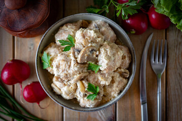 Hearty dinner: meatballs in cream sauce on a plate on a wooden background. View from above