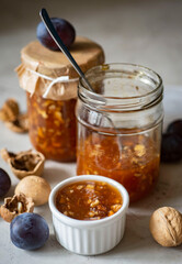 Plum jam with walnuts in a glass jar on a beautiful gray background. Vertical photo. Close-up