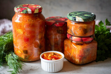 Pickled vegetable salad in a glass jar on a gray background. Close-up