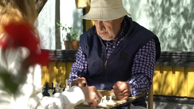 Senior man and young woman playing chess in the garden. Leisure activity, mental health and full life in old age, sport, entertainment, old generation, happy active retired people, healthcare and