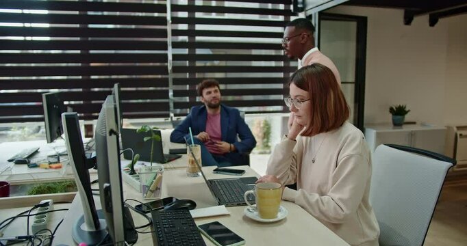 Young diverse male colleagues discuss project challenges, a woman enhances the collaboration by searching for information online, contributing to a dynamic and inclusive workplace