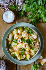 Hearty lunch: Pasta with shrimp in cream sauce with parmesan cheese in a beautiful green plate on wooden planks. Vertical photo. Close-up.