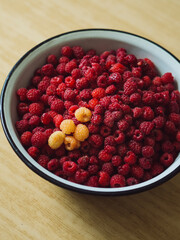 Red and yellow raspberries in a metal bowl on a table. A vertical close-up straight from above shot.