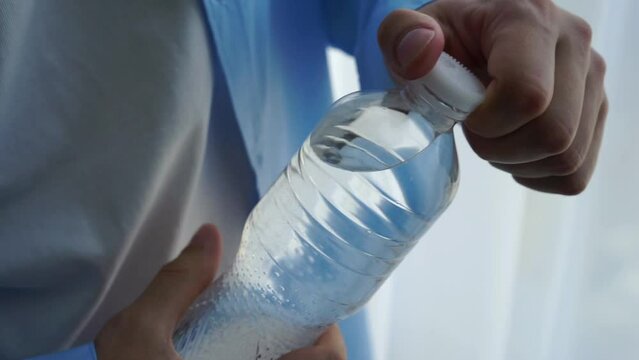 a man opens a plastic bottle of water.
Man holding a bottle of water in his hands